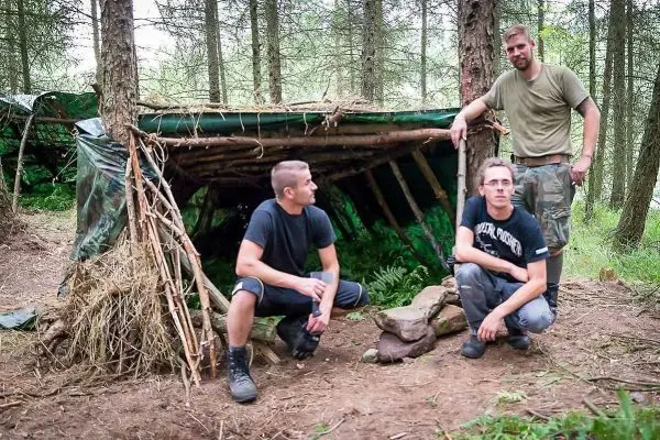 Selbstgebaute Tarp-Notunterkunft aus Ästen und Blättern im Wald