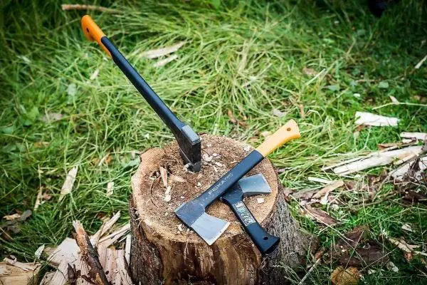 Zwei Äxte liegen auf einem Baumstumpf im Gras