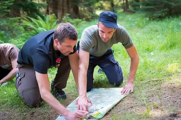 Zwei Personen analysieren eine Karte auf dem Boden im Wald