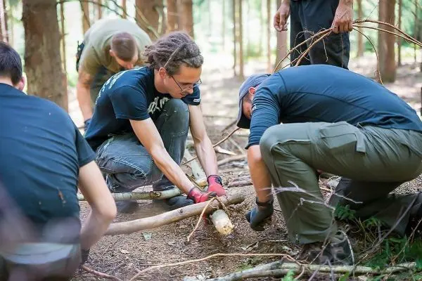 Zwei Personen bauen eine Holzstruktur im Wald aus Ästen und Stöcken