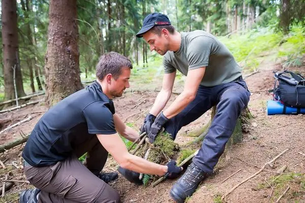 Zwei Personen bauen eine kleine Struktur aus Ästen im Wald