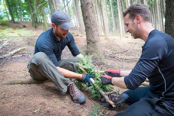 Zwei Personen bauen eine Struktur aus Ästen im Wald