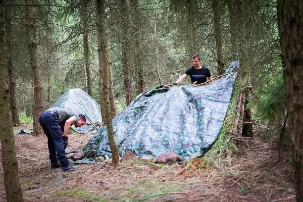 Zwei Personen bauen eine Tarp-Notunterkunft im Wald auf