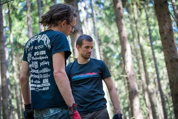 Zwei Personen betrachten den Boden im Wald, umgeben von Bäumen