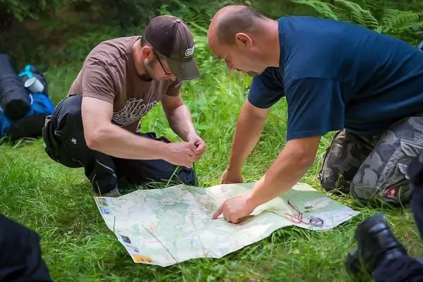 Zwei Personen betrachten eine Karte auf dem Boden im Grünen beim Überlebenstraining