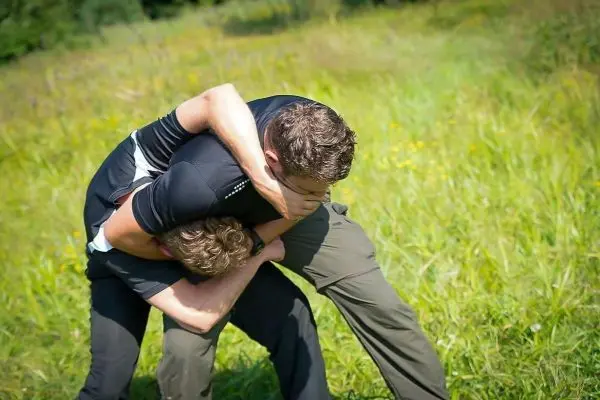 Zwei Personen führen eine körperliche Auseinandersetzung im hohen Gras durch