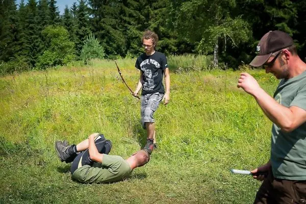 Zwei Personen im Gras, eine steht mit Stock, eine liegt am Boden