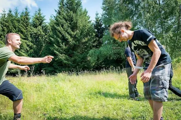 Zwei Personen interagieren auf einer Wiese, eine Person zeigt auf die andere