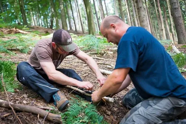 Zwei Personen konstruieren eine Schlagfalle im Wald aus Ästen und Seil