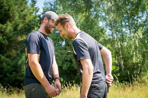 Zwei Personen stehen in einer Wiese und lachen miteinander