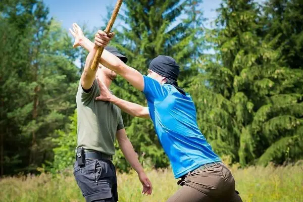 Zwei Personen üben eine Selbstverteidigungstechnik mit einem Stock im Freien