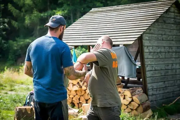 Zwei Personen üben eine Technik zur Selbstverteidigung in der Nähe einer Holzunterkunft