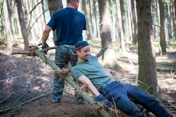 Zwei Personen ziehen an einer improvisierten Trage aus Ästen im Wald