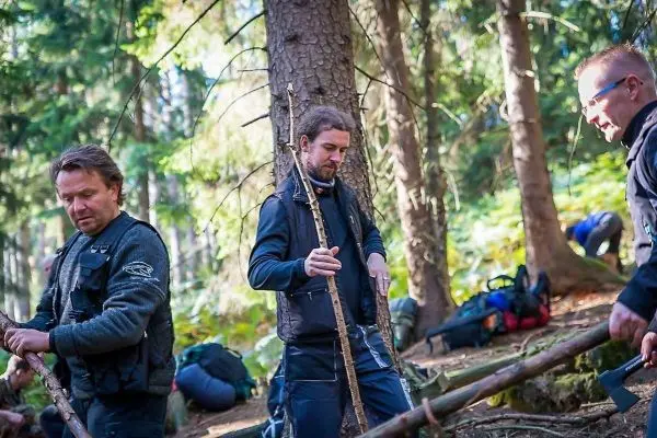 Drei Personen bearbeiten Äste im Wald, während Rucksäcke im Hintergrund liegen