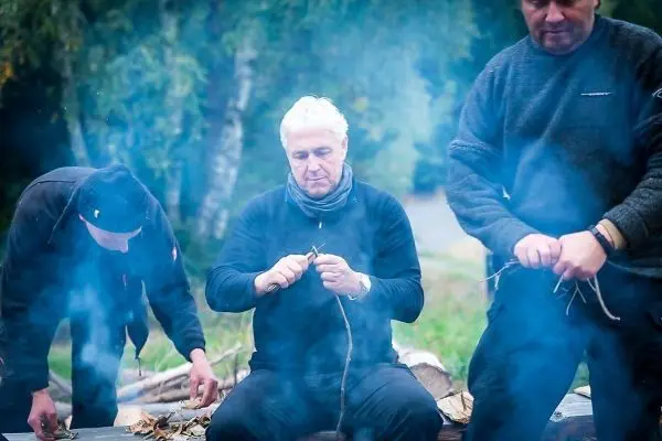 Drei Personen bereiten Zunder aus Blättern und kleinen Ästen vor