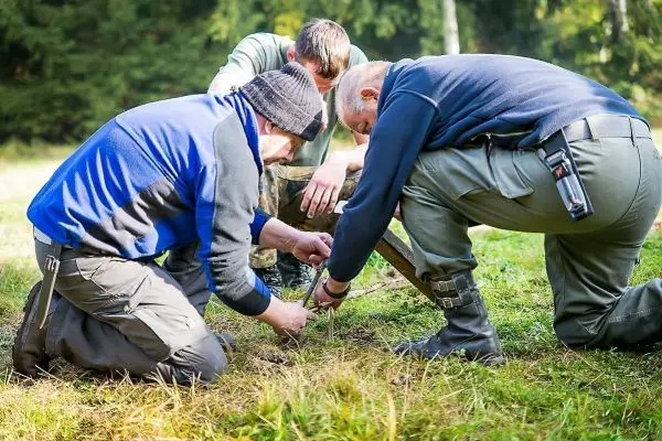 Drei Personen knien im Gras und arbeiten an einer Holzstruktur