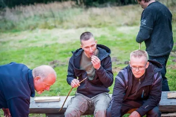 Drei Personen sitzen an einem Tisch und arbeiten mit Holzstücken