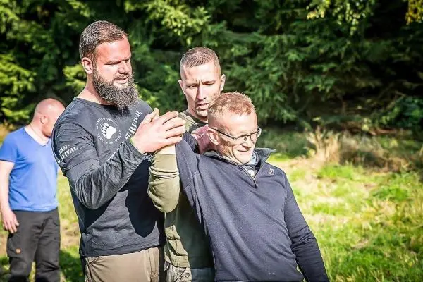 Drei Personen üben eine Technik zur Unterstützung oder Rettung im Freien