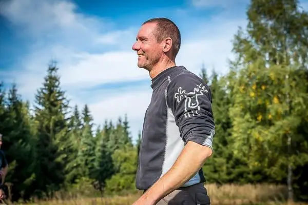 Ein Mann steht lächelnd im Freien, umgeben von Bäumen und Gras