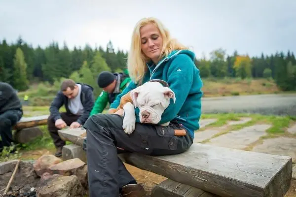Frau sitzt auf Holzbank und hält schlafenden Hund im Arm