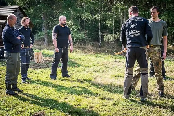Fünf Personen stehen auf einer Wiese und beobachten eine Demonstration mit einem Holzstück