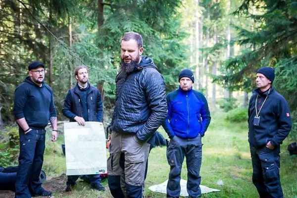 Fünf Personen stehen im Wald und betrachten eine Karte