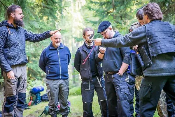 Gruppendiskussion im Wald mit mehreren Personen und Rucksäcken im Hintergrund