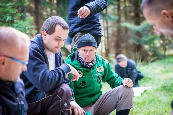 Gruppendiskussion im Wald, Teilnehmer sitzen auf dem Boden und betrachten Materialien