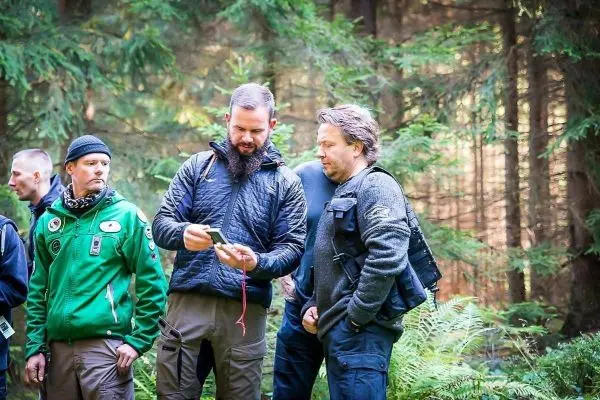 Gruppendiskussion im Wald über Ausrüstung und Technik, Teilnehmer betrachten ein Gerät
