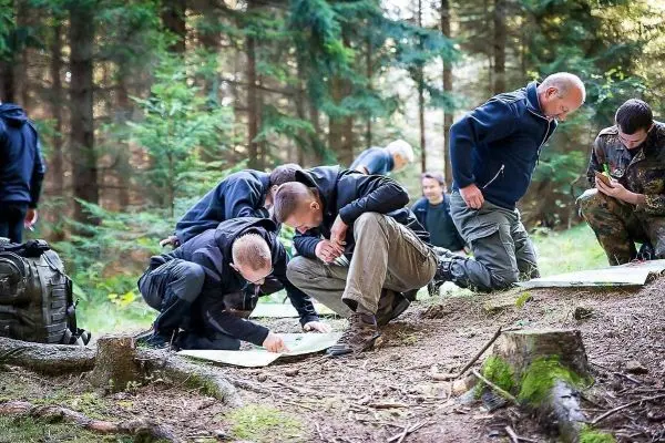 Gruppenmitglieder studieren Karten im Wald, einige knien auf dem Boden