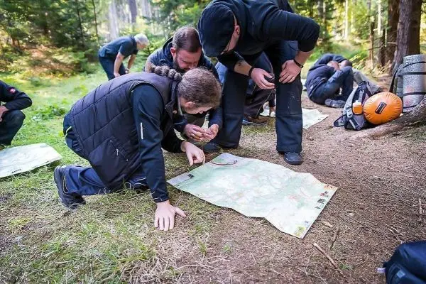 Gruppierung betrachtet Karte auf dem Boden im Wald, einige Personen knien
