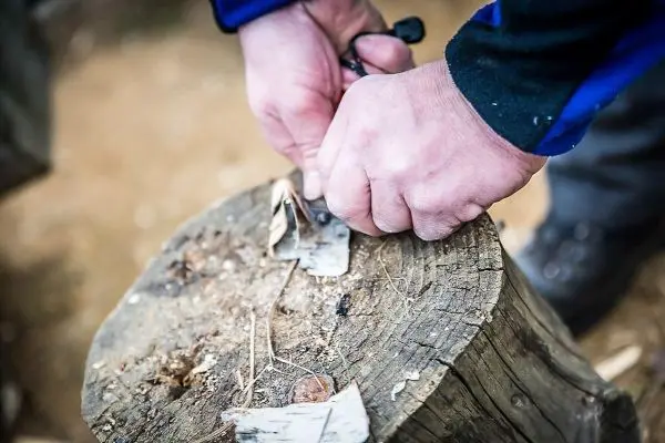 Hände bearbeiten Zunder auf einem Baumstumpf mit einem Messer