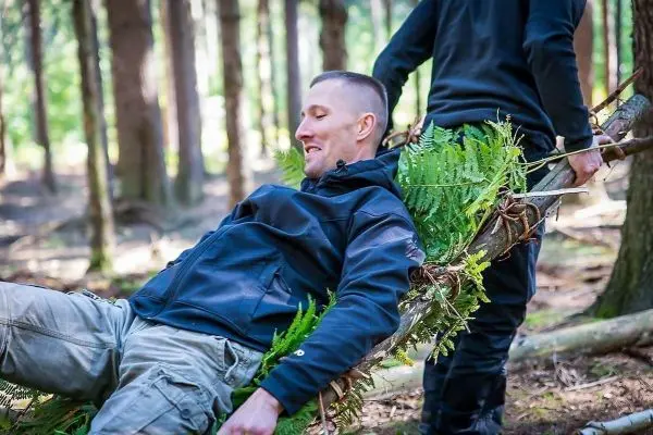 Improvisierte Trage aus Ästen und Farn transportiert Person im Wald