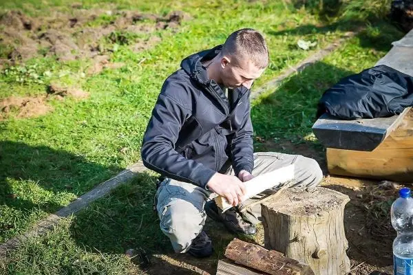 Mann bearbeitet Holzstück mit einem Messer auf einem Baumstumpf