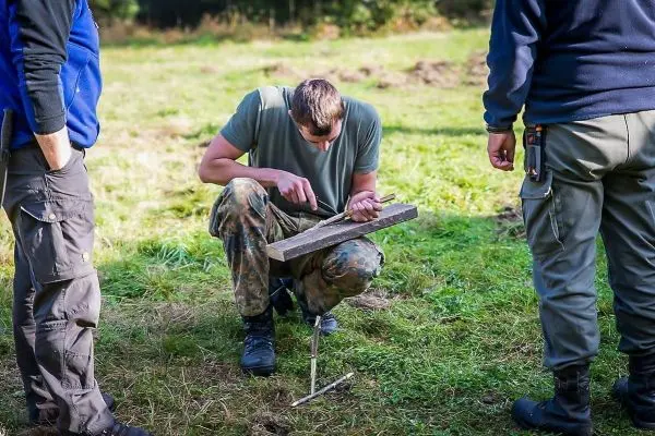 Mann bearbeitet Holzstück mit Messer auf improvisierter Werkbank