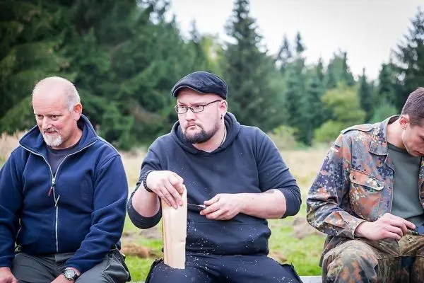 Mann bearbeitet Holzstück mit Messer, Holzspäne fallen auf den Boden