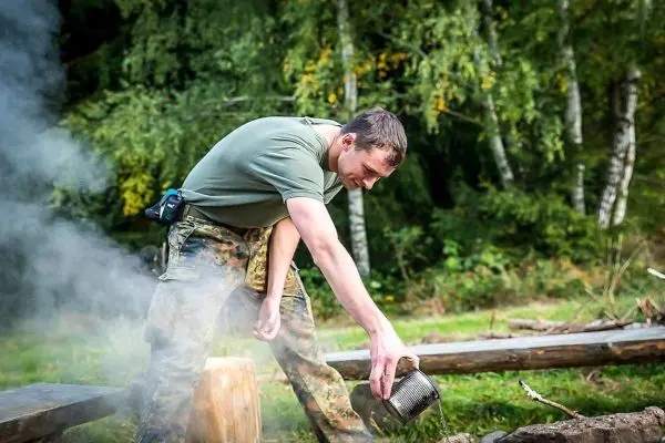 Mann gießt Wasser aus einem Behälter über ein kleines Bodenfeuer