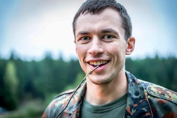 Mann hält einen Stock im Mund und lächelt in die Kamera