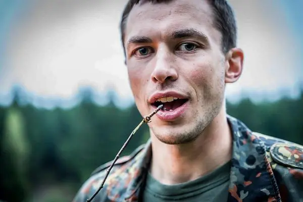 Mann hält einen Stock im Mund und schaut in die Kamera