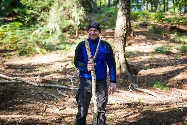Mann hält einen Stock in einem Waldgebiet mit Laub und Bäumen