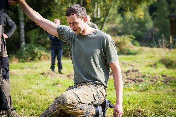 Mann kniet auf dem Boden und hebt eine Hand in Richtung einer anderen Person