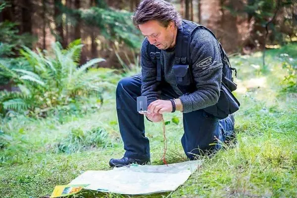 Mann kniet auf Gras und nutzt einen Kompass über einer Karte