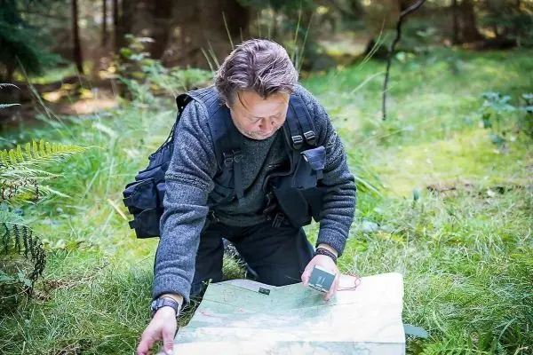 Mann kniet im Gras und studiert eine Karte mit Kompass in der Hand
