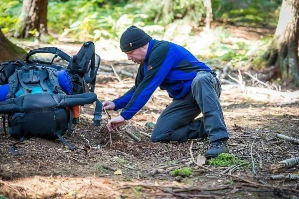 Mann kniet im Wald und sammelt Äste für eine Konstruktion