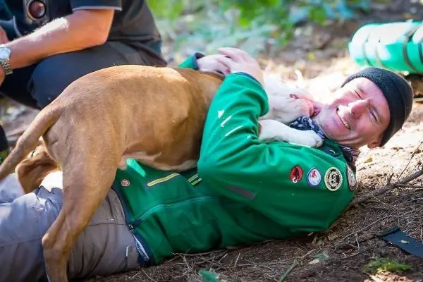 Mann liegt auf dem Boden und umarmt einen Hund