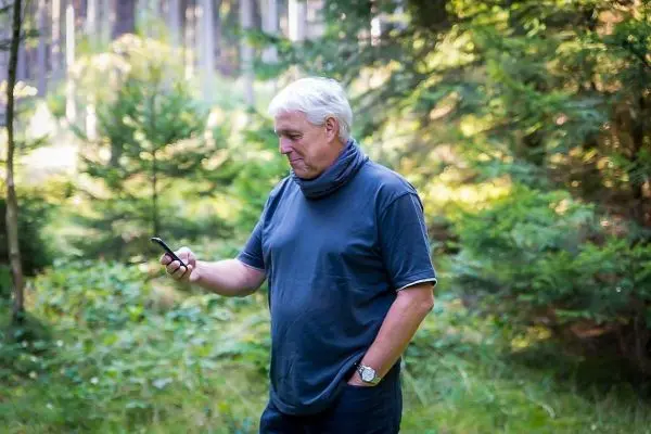 Mann steht im Wald und schaut auf sein Smartphone