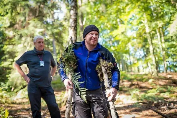 Mann trägt zwei Äste mit Farnen durch den Wald