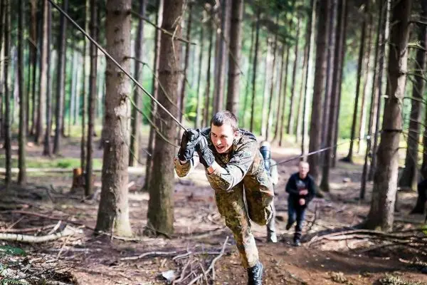 Mann überquert selbstgebaute Seilbrücke im Wald, während andere folgen