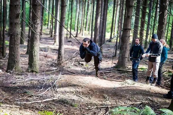 Mann überquert selbstgebaute Seilbrücke zwischen Bäumen, andere beobachten