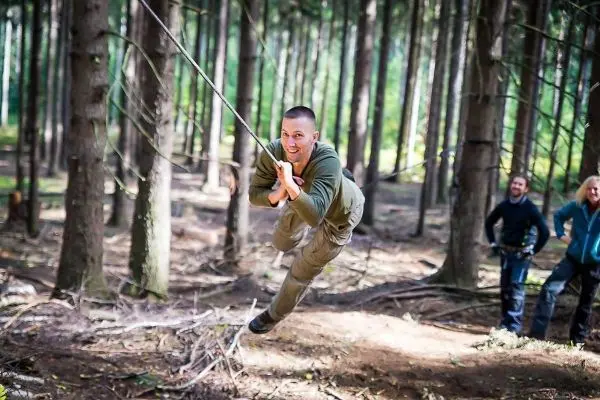 Mann überquert selbstgebaute Seilbrücke zwischen Bäumen im Wald